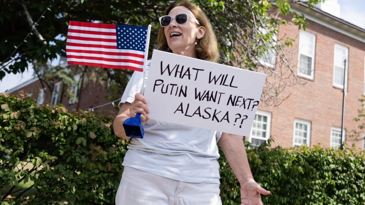 A woman dressed in all white is holding an American flag and a poster that reads: 'What will Putin want next? Alaska??'