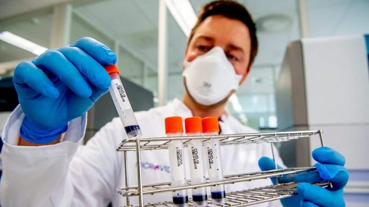 Man wearing face masks and gloves holding up COVID-19 test vials