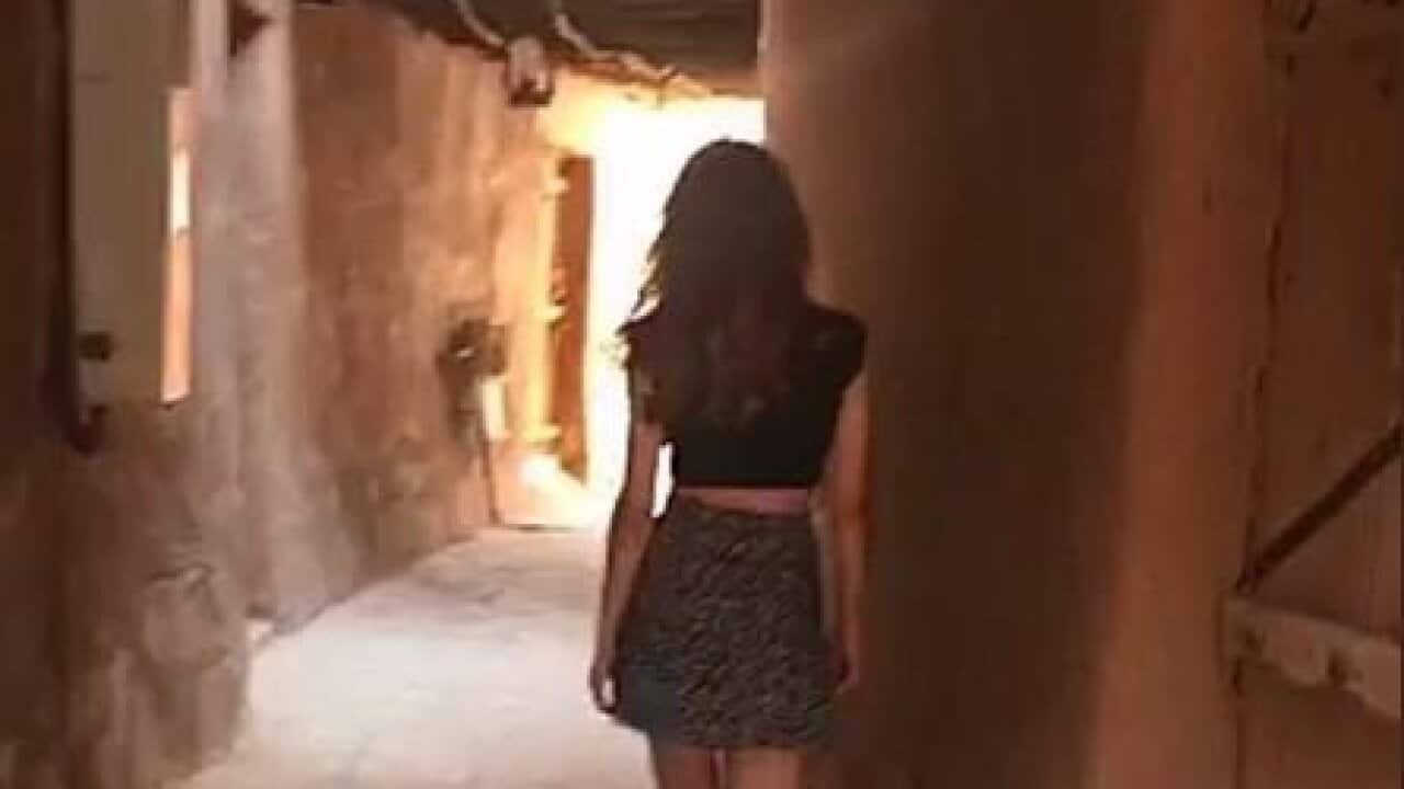 A still from a video of a woman wearing a skirt and t-shirt in public.