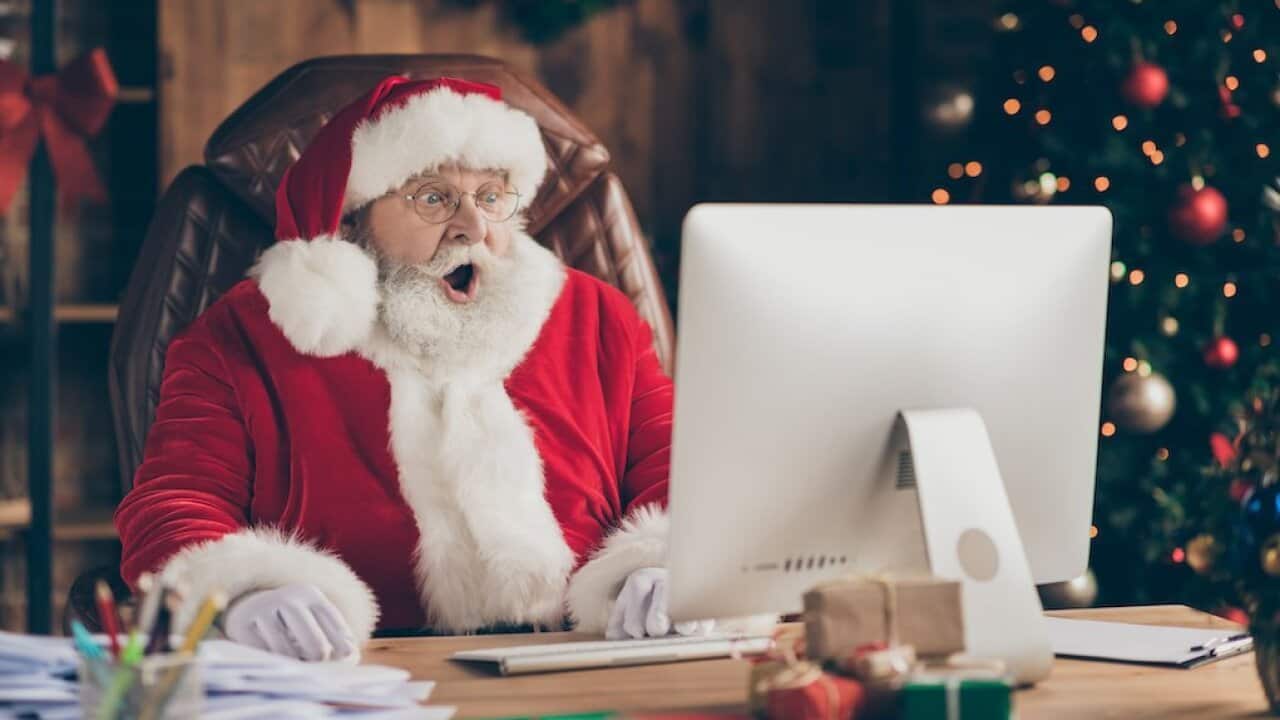 Photo of amazed santa claus sit table desk work computer impressed many wish gift list letters in house idnoors with evergreen christmas x-mas tree ornament decoration wear cap headwear