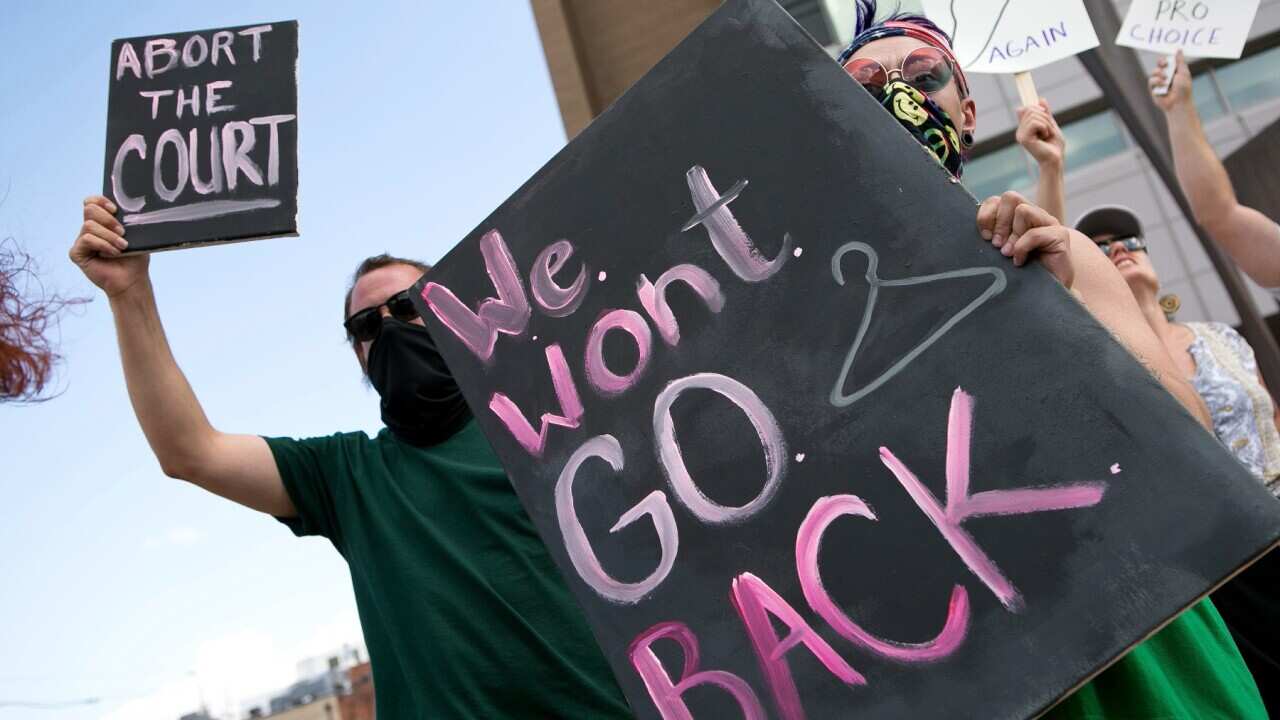 Protesters holding a sign that says "We won't go back" with a coathanger