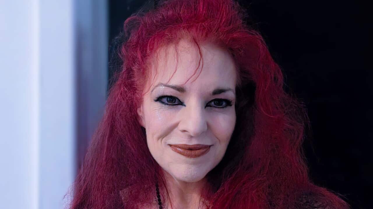 a close up of a middle aged woman with long red hair wears black gothic clothes, accessories and makeup
