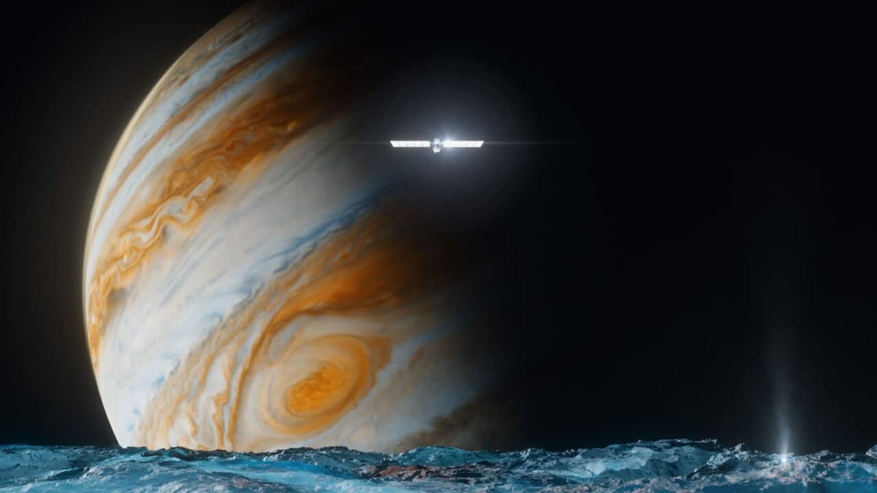 The illustration provided by NASA depicts the Europa Clipper spacecraft above the surface of the moon Europa, foreground, and Jupiter behind. (NASAJPL-Caltech via AP)