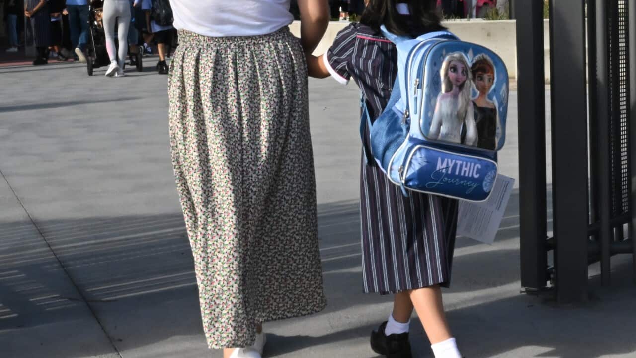A woman wearing a long floral skirt holding a child's hand. They both have their back turned.