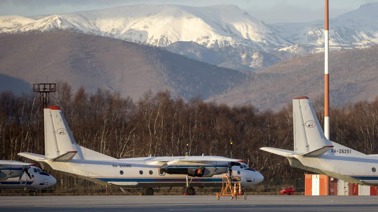 An aeroplane on a tarmac, with hills in the background.