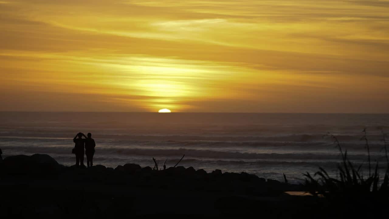 Tourists watch the sunset on the horizon at Hokitika in New Zealand