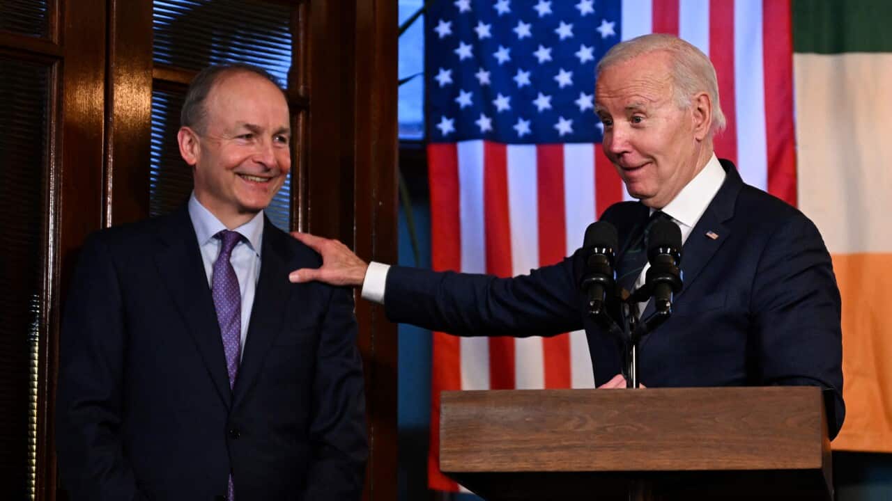 US President Joe Biden places his hand on the shoulder of Irish foreign minister Micheal Martin. The US and Irish flags are hanging from the ceiling behind them.