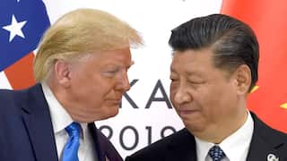 Two men in suits stand close together during a diplomatic meeting, with US and Chinese flags visible in the background.
