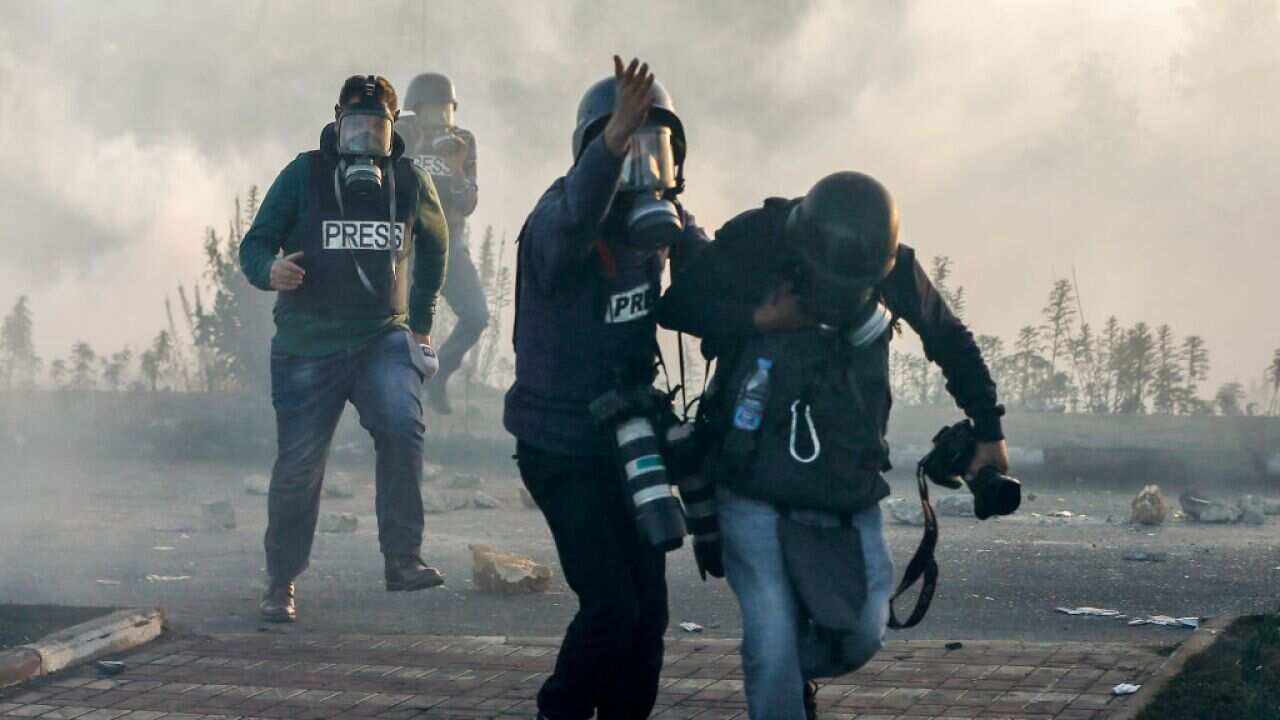 Photojournalists and video journalists wearing gas masks flee from teargas fired by Israeli forces on the West Bank.