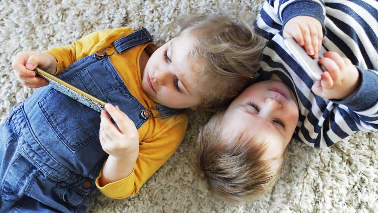 Brother and sister laying down looking at phones