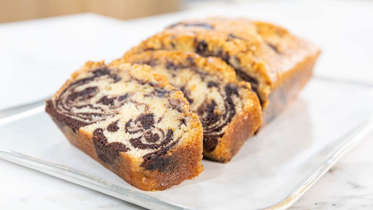 A loaf cake sits on a white board. Several slices have been cut, and sit on an angle at the front, showing the choc-vanilla swirls inside the cake.