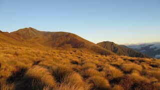 A photo of mountains close to the town of Te Anau in New Zealand. Brown grass covers the hilltops into the distance.
