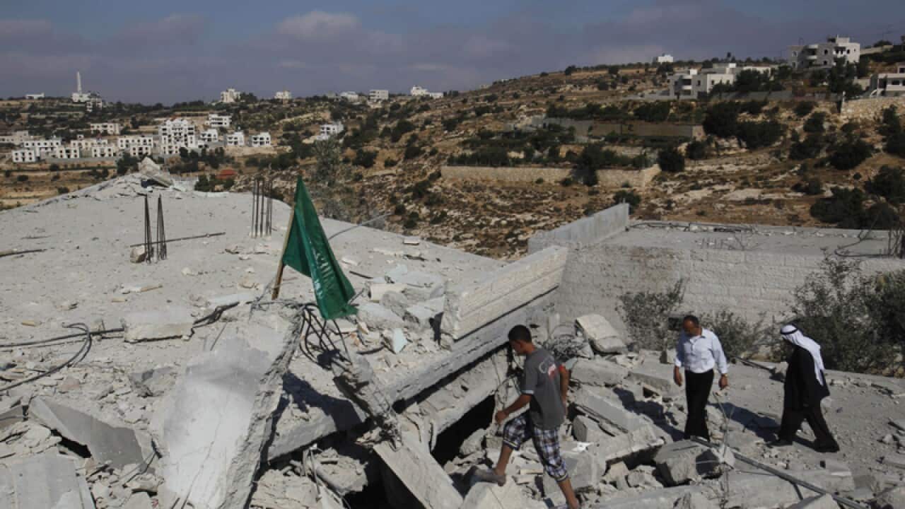 Palestinians walk in the rubble of a house