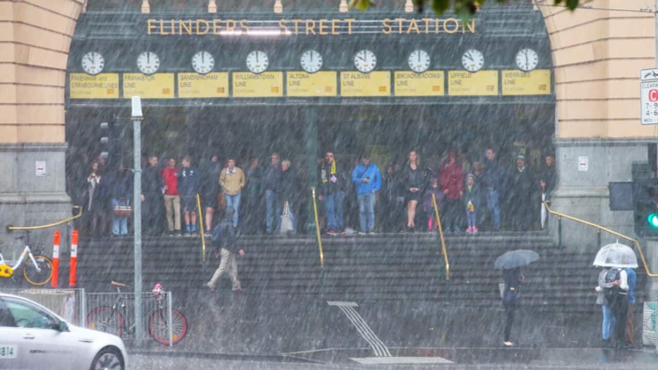 People are seen in Flinders Street, Melbourne, Saturday, April 14, 2018. Strong, squalling winds and heavy rain are lashing Melbourne as a series of cold fronts move across Victoria. (AAP Image/David Crosling) NO ARCHIVING