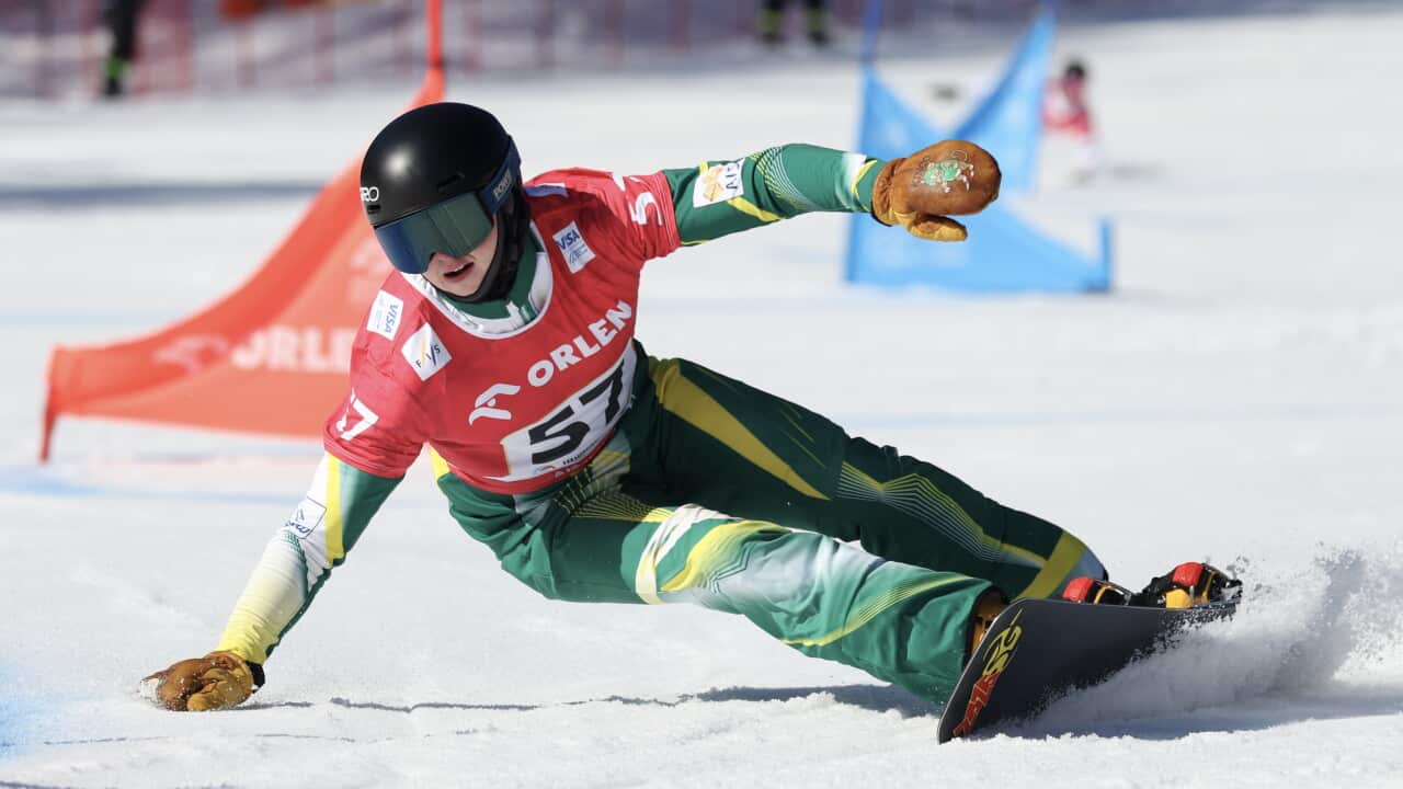 Harvey Edmanson snowboarding, he is almost parallel to the ground with one hand on it and the snowboard kicking up a puff of snow.