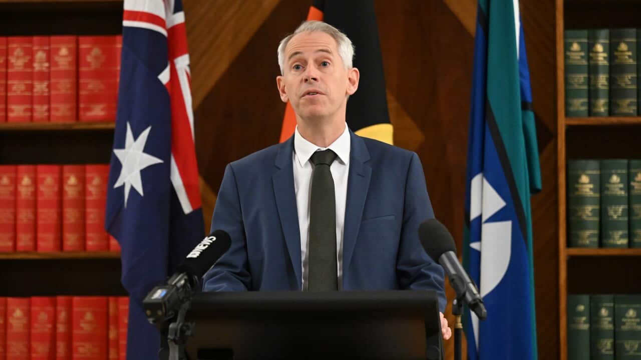 Andrew Giles stands at a podium in front of the Australian, Aboriginal and Torres Strait Islander flags.
