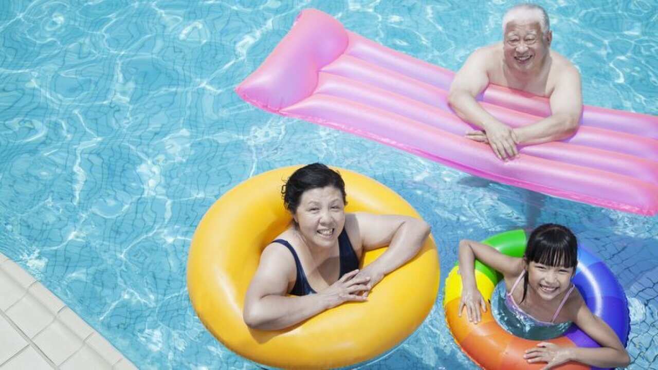 Multi-generational family playing in the pool with inflatable tubes, looking at camera