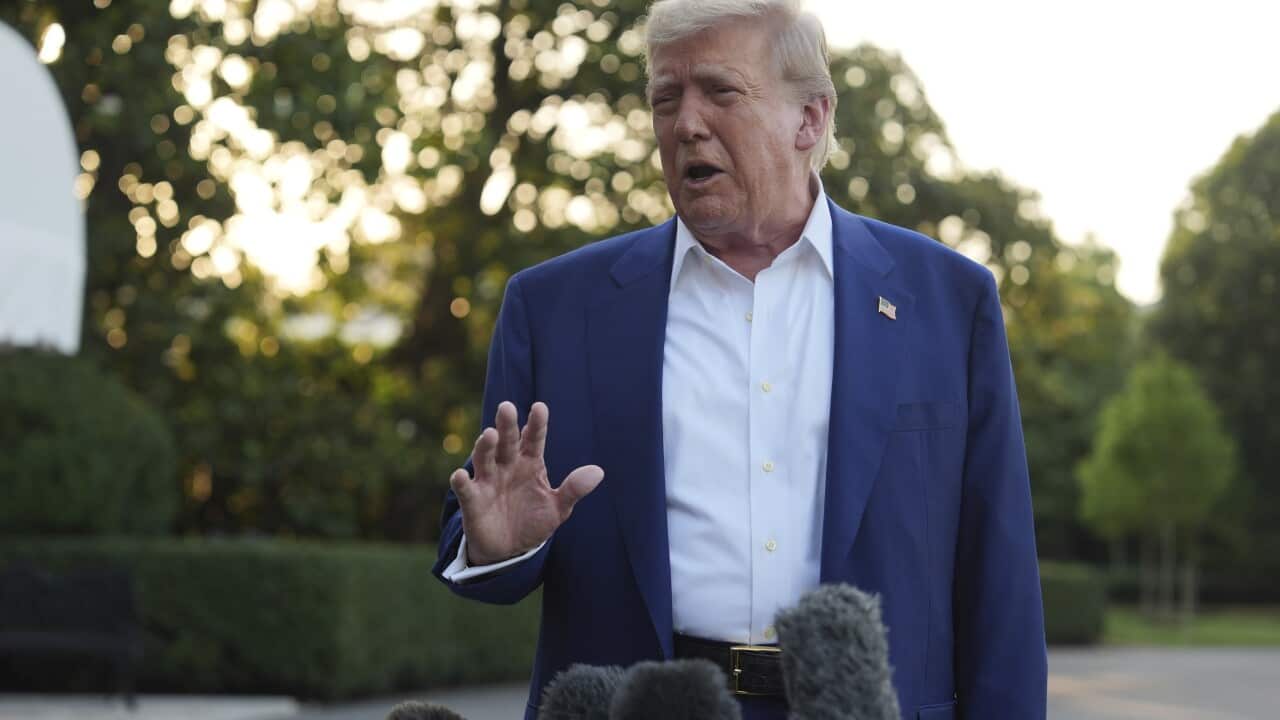 A man in a blue blazer and white shirt, speaking in front of a lawn.
