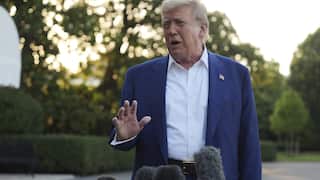 A man in a blue blazer and white shirt, speaking in front of a lawn.