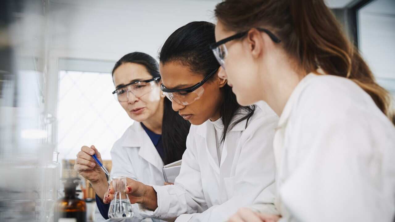 Female chemistry teacher explaining to young multi-ethnic students in laboratory