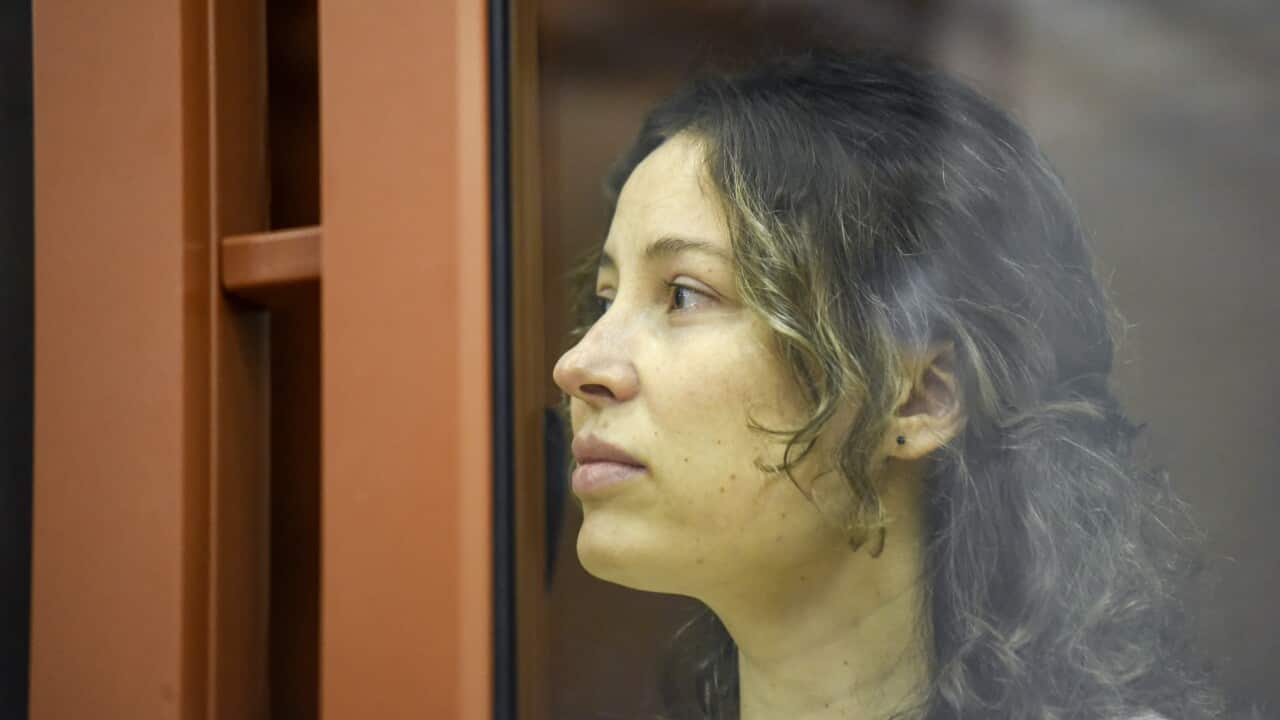 A woman sits in a glass cage in a courtroom