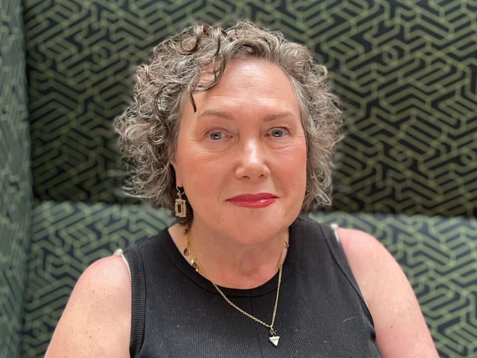 a closeup shot of a middle aged woman with grey hair sits on a green and black geometrically patterned couch