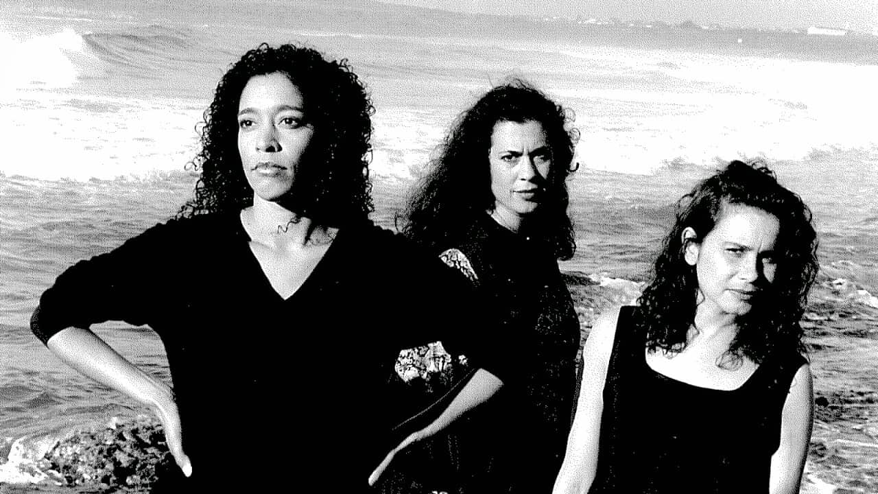Three women posing by the ocean for a photo.