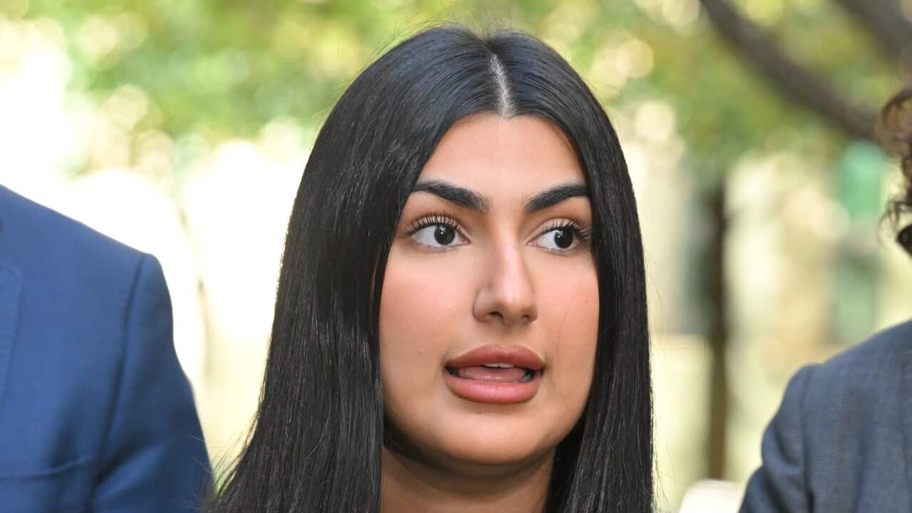 A woman's face, taken while she is speaking flanked by two others.