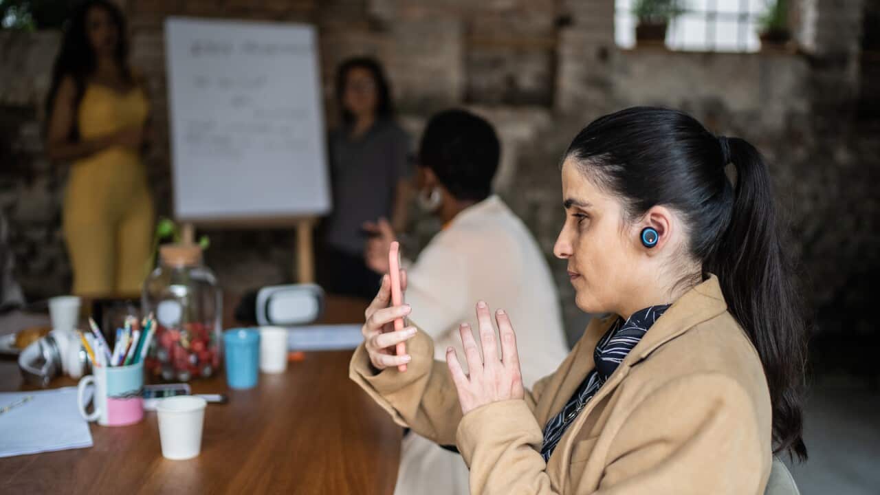 Visually impaired businesswoman using smartphone and earphones during business meeting