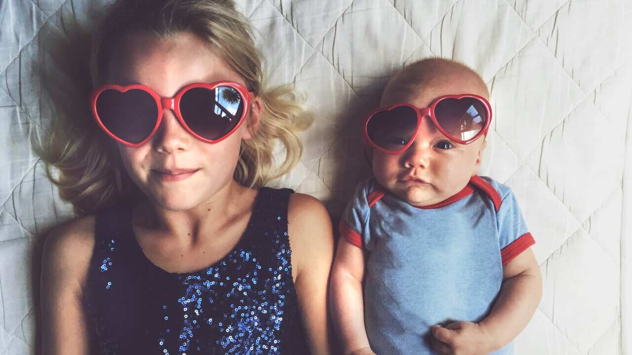Young girl and baby laying beside each other wearing love heart glasses