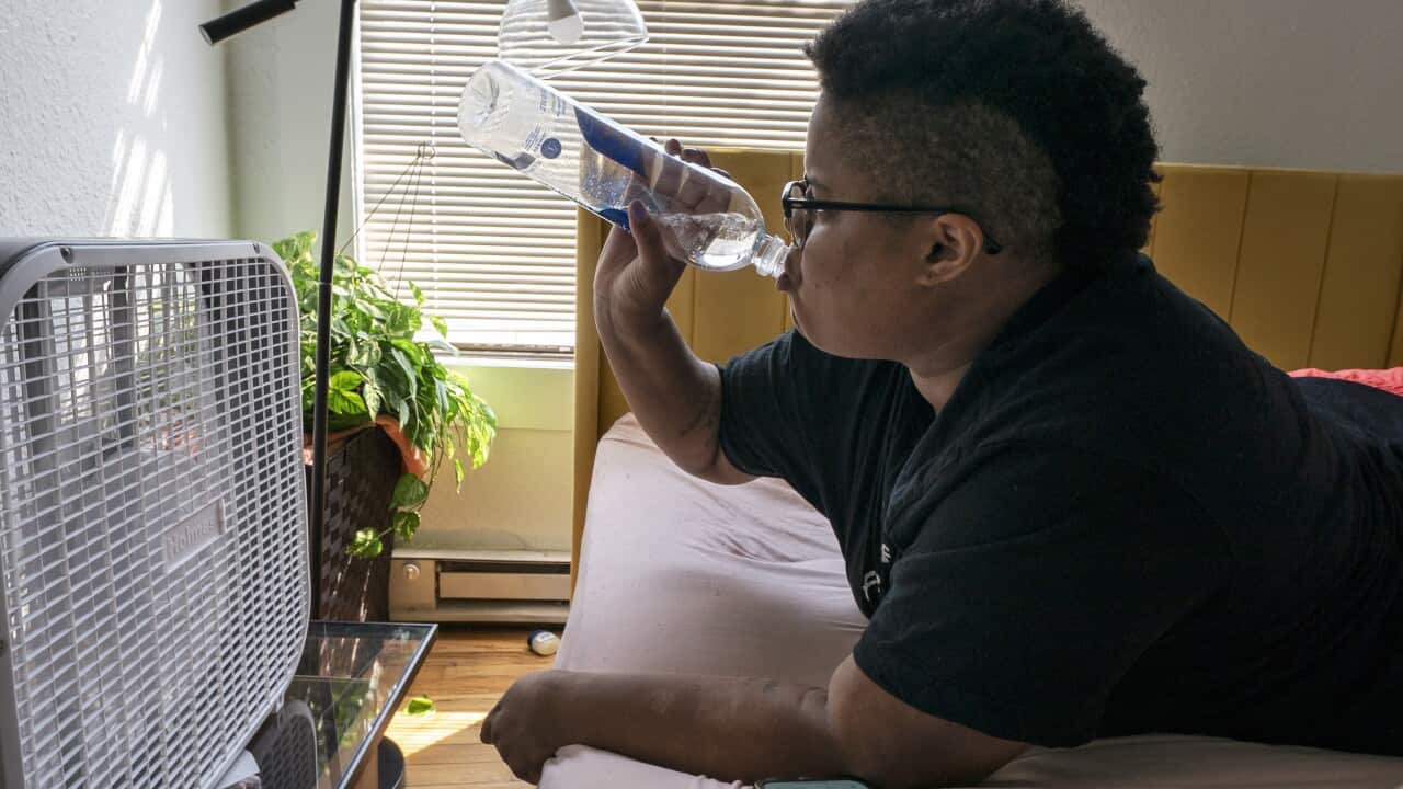A person sits in front of a box fan with a water bottle.