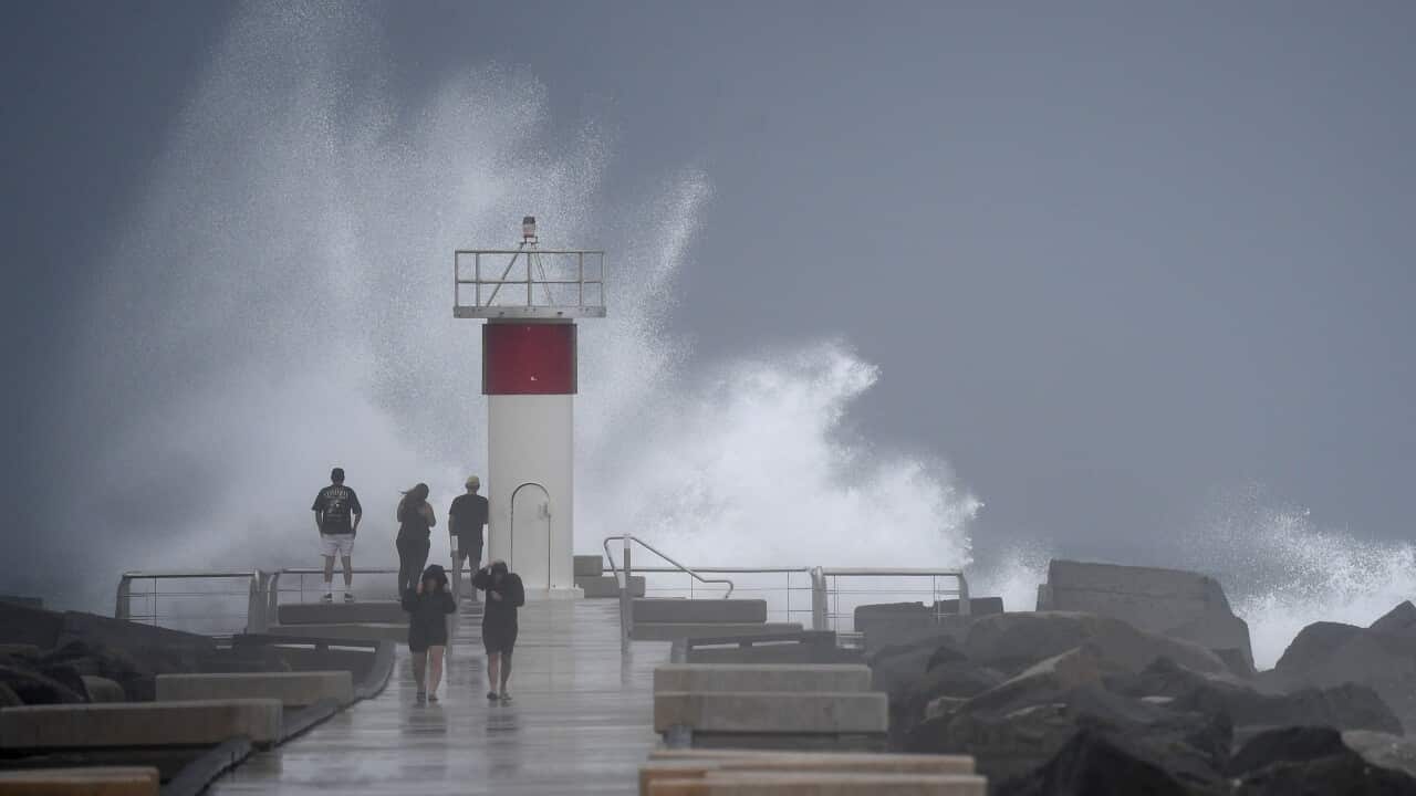 People walking near a lighthouse as waves are crashing onto the rocks
