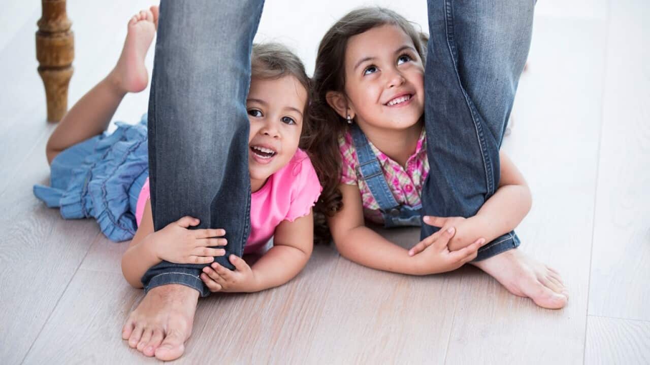 Playful girls holding father's legs on hardwood floor