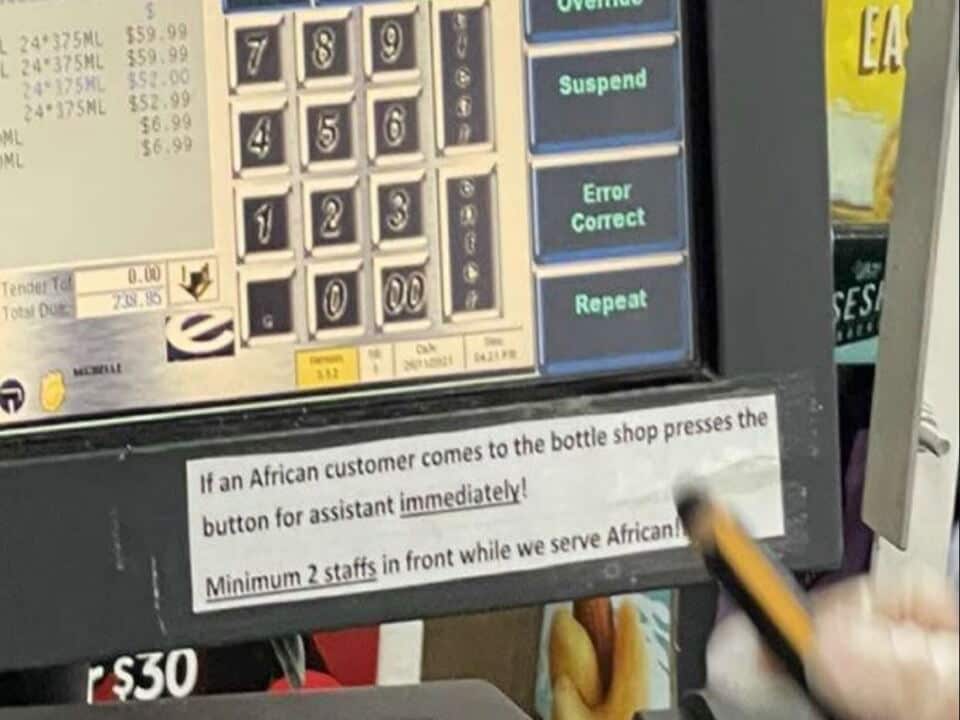 A sign displayed on a cash register at a Melbourne IGA reading 'If an African customer comes to the bottle shop presses the button for assistant immediately!'