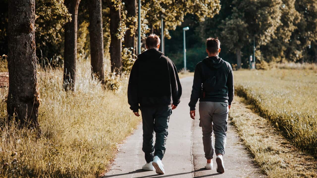 Two young men walking on a footpath outside facing away from camera