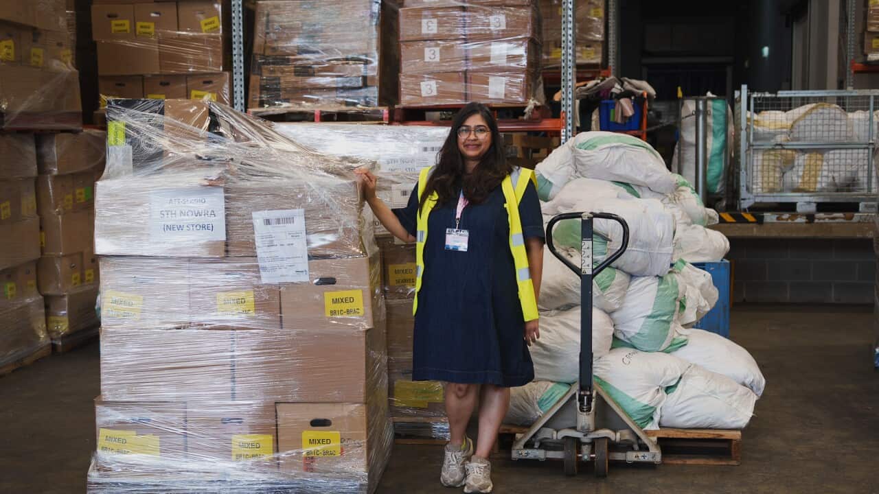 A woman is posing in front of large stacks of boxes and bags filled with donated clothing
