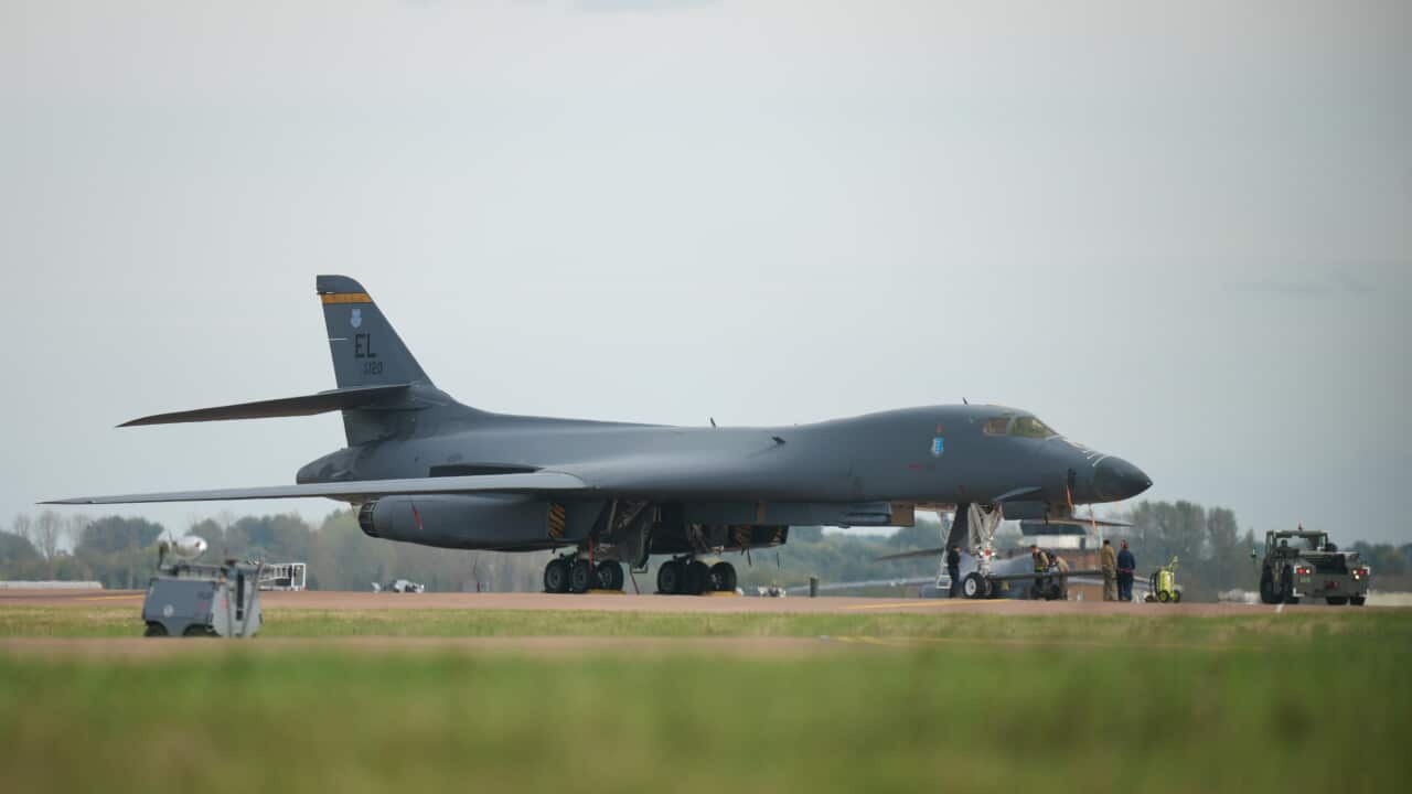 Large military bomber aircraft parked on an airfield, with ground crew and support vehicles positioned beside the aircraft on the tarmac.