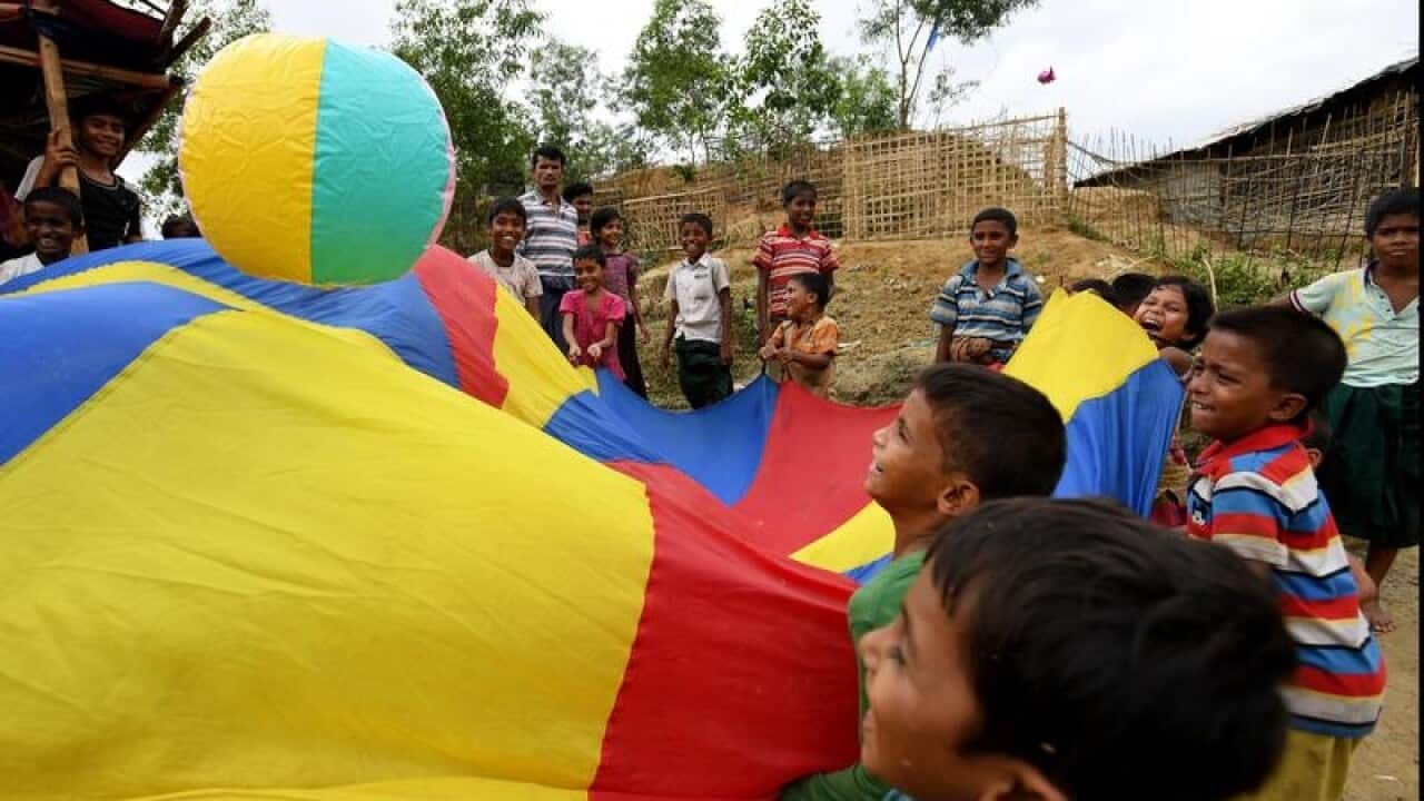 Rohingya children play with a ball on a multicoloured sheet.