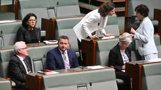 A group of MPs seated in parliament. They include two men in suits, beside another woman. Two other women are standing behind them.
