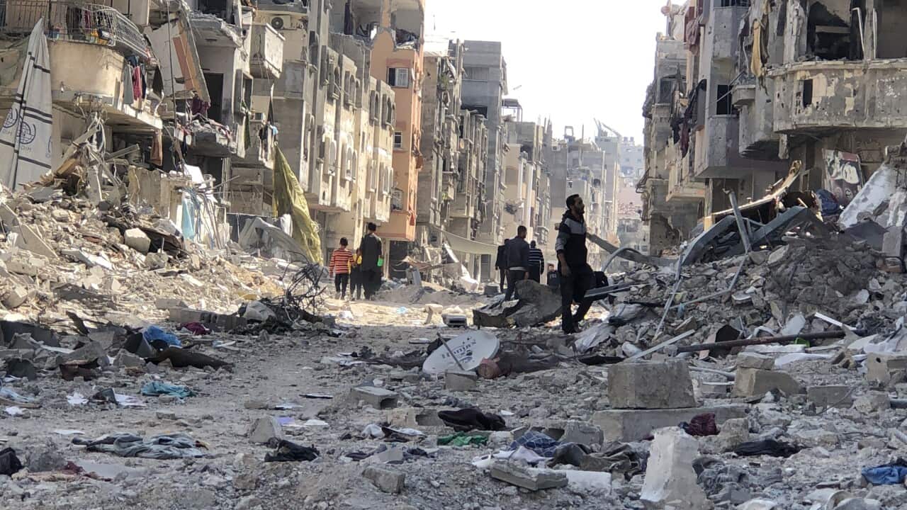 People walking past the rubble of destroyed buildings.