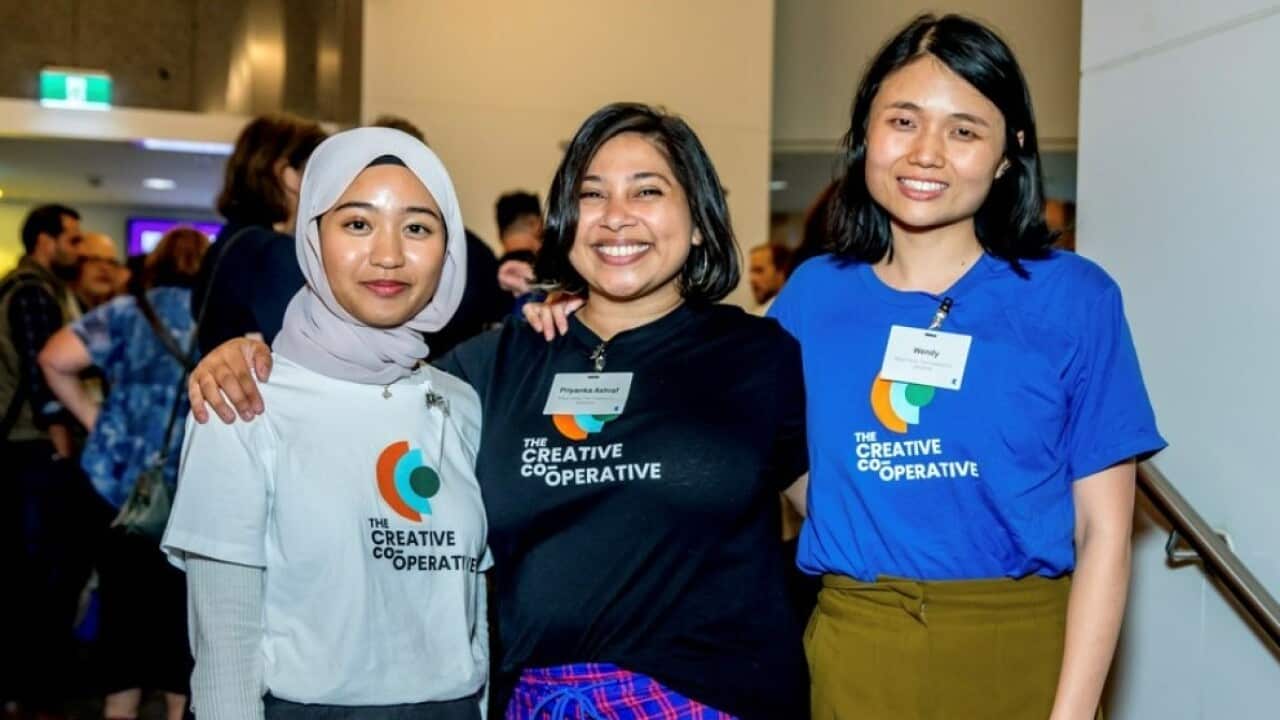Three women stand with their hands on each other's shoulders.