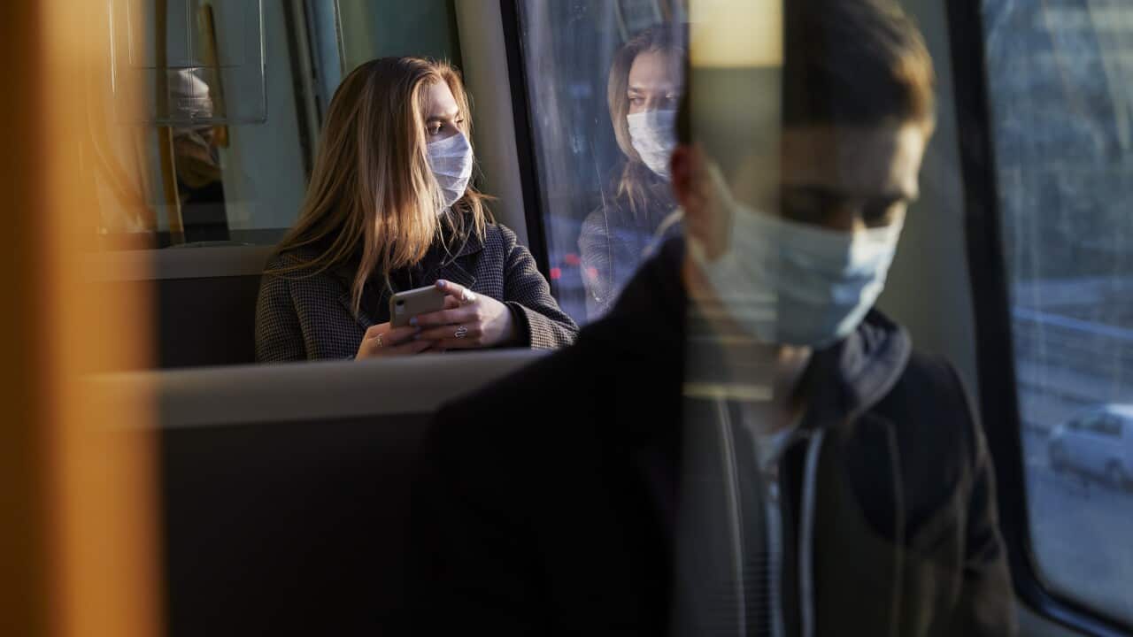 young woman sitting in train wearing protective mask, using smartphone