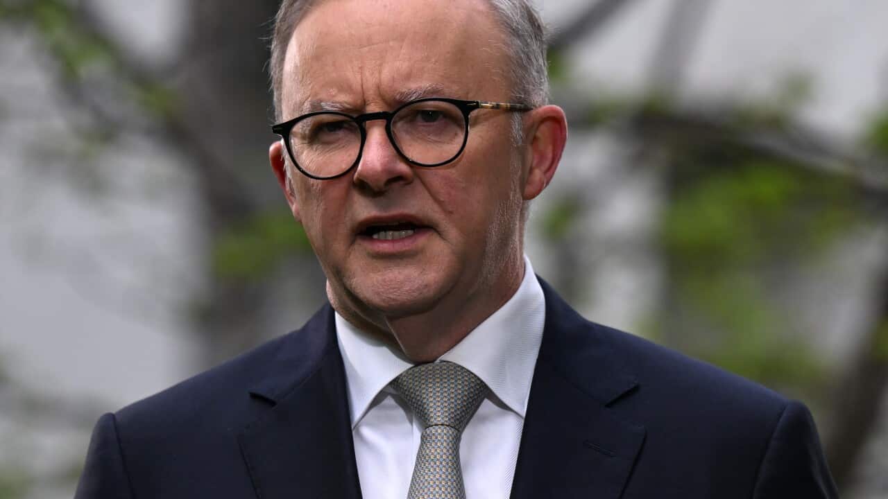 A man wearing a suit, tie and glasses speaking.