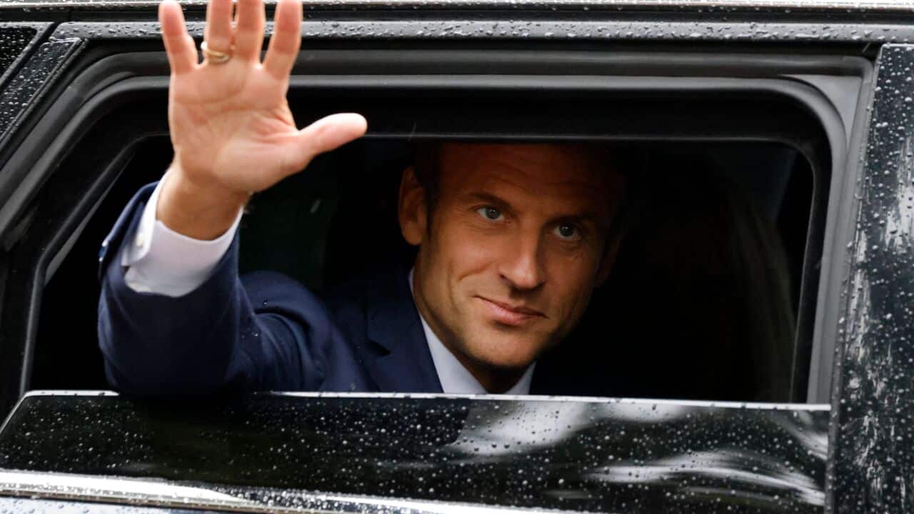 Man waves from the back seat of a car, with his hand outstretched from the window.