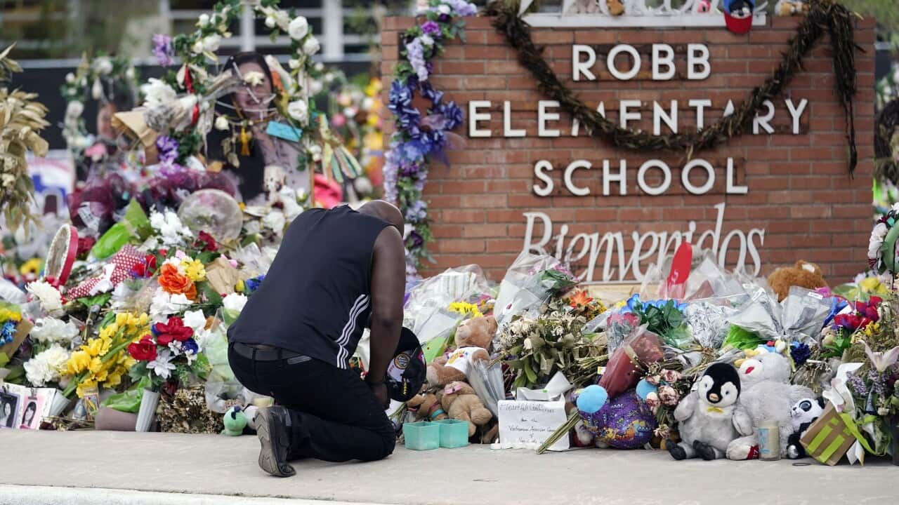 A man kneels at a flower memorial