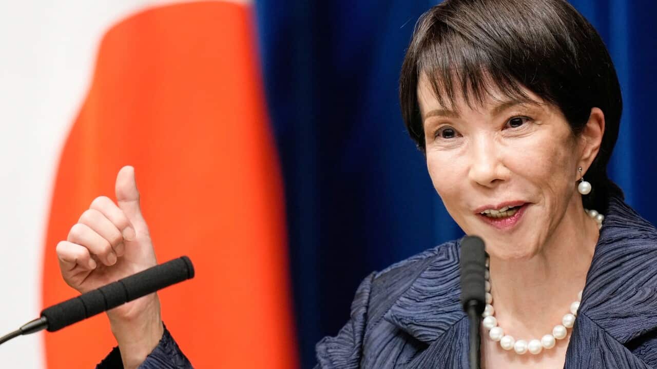 A woman speaks at a press conference with a Japanese flag behind her.