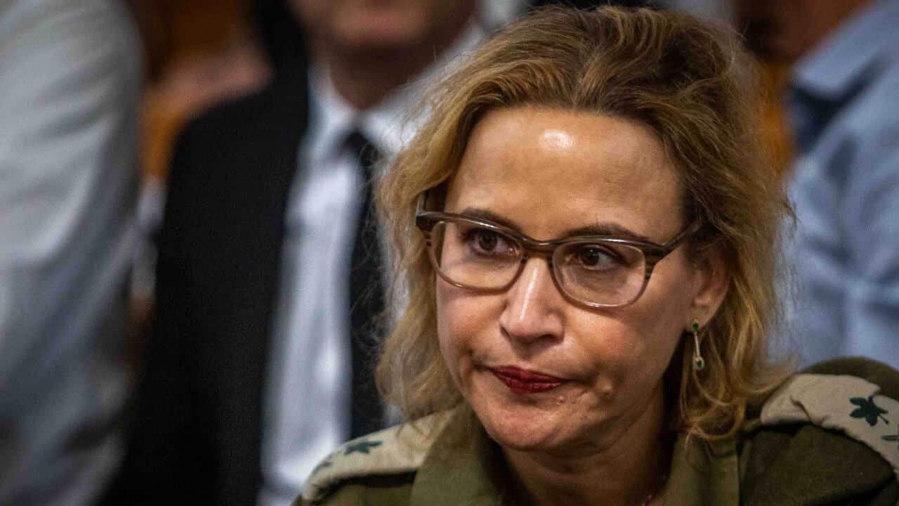A woman in military attire and wearing glasses looks on at a meeting.