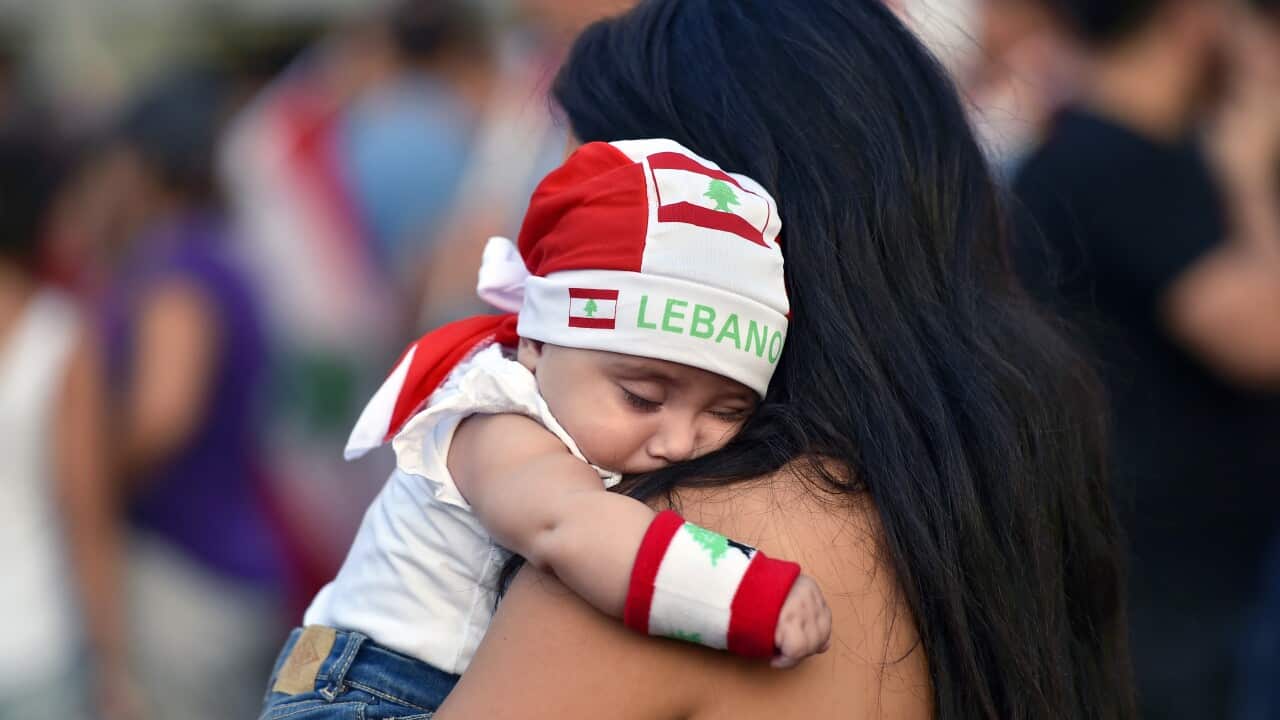 A woman carries her child as he wears a headband with the national flag during a protest in Jal El Dib area north of Beirut, Lebanon, 22 October 2019.