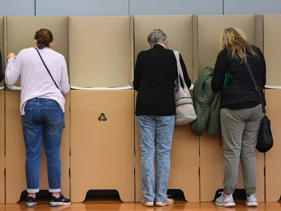 People standing at voting booths filling out ballot papers.