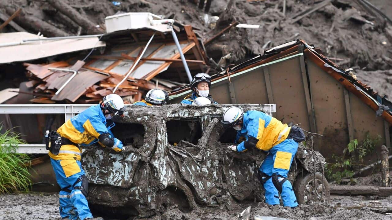Rescuers check a damaged vehicle at the site of a mudslide in Atami, Shizuoka prefecture,